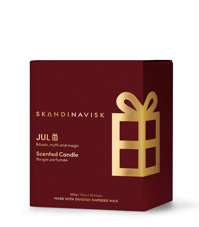 A burgundy box containing the Skandinavisk Seasonal Scented Candle Jul Gold Symbol, 200 g, adorned with gold gift and text designs that highlight its Scandinavian-inspired branding. Crafted with Swedish rapeseed wax, this gingerbread-scented candle evokes the cozy warmth and festive spirit of a Nordic holiday season.