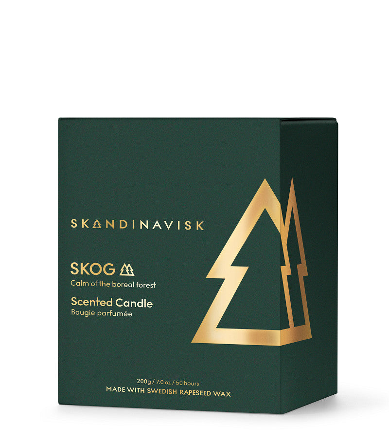 A dark green box of Skandinavisk Seasonal Scented Candle Skog Gold Symbol, 200 g, featuring a gold tree graphic and text. Inspired by the tranquility of boreal forests, this candle is crafted from Swedish rapeseed wax and captures the fresh scent of pine needles. Net weight: 200 g/7.0 oz; burn time approx. 50 hours.