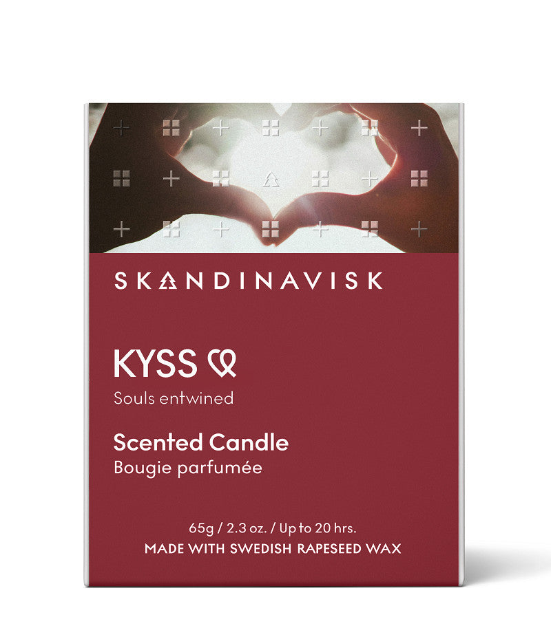 The Skandinavisk Scented Candle Kyss, 65g, comes in a maroon box with two hands forming a heart against a sunset and "Souls entwined" text. Includes a Swedish rapeseed wax candle with engraved beechwood lid.