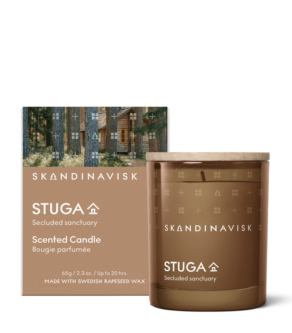 A 65 g Seasonal Scented Candle Stuga by Skandinavisk, housed in a brown glass container with a wooden lid, is displayed before its box adorned with artwork of a wooden house nestled in the forest. Infused with the earthy aroma of woodland mosses, this candle is crafted from Swedish rapeseed wax and elegantly packaged to capture the serene essence of Scandinavian nature.