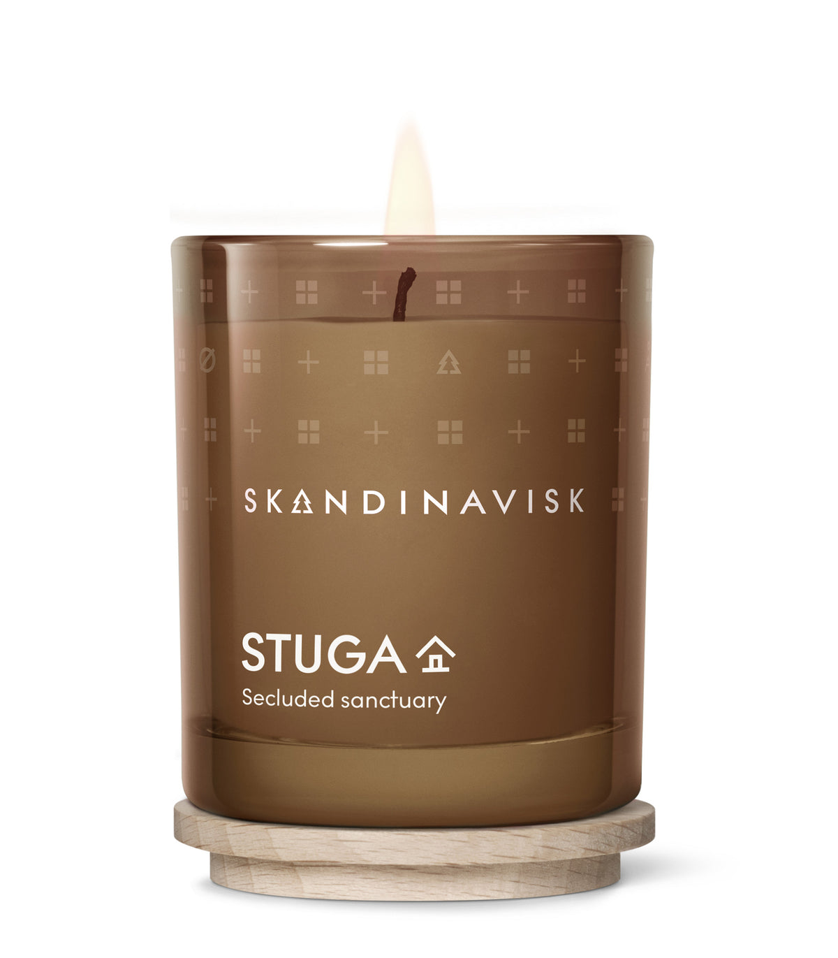 A 65g Skandinavisk Seasonal Scented Candle Stuga in brown glass burns on a round wooden base. Crafted from Swedish rapeseed wax and delicately scented with birch bark and woodland mosses, the candle’s glass is adorned with subtle icons of houses and trees.