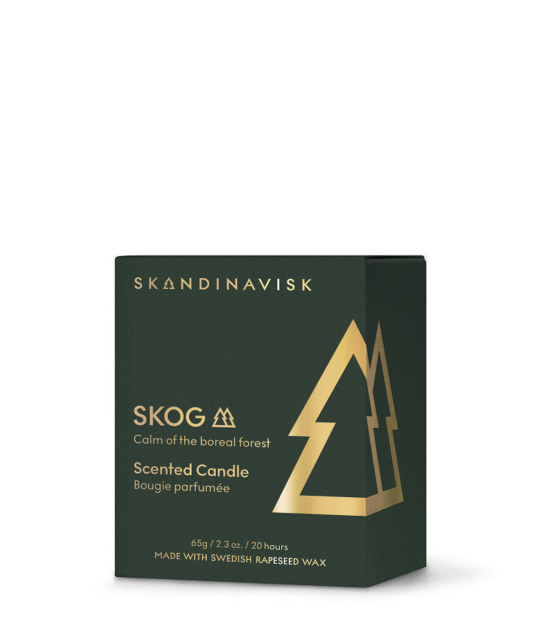 A dark green box of Skandinavisk Seasonal Scented Candle Skog Gold Symbol, 65 g, featuring gold tree graphics and text. The label highlights the calm of the boreal forest, notes its pine needle scent, and states that it is made with Swedish rapeseed wax.