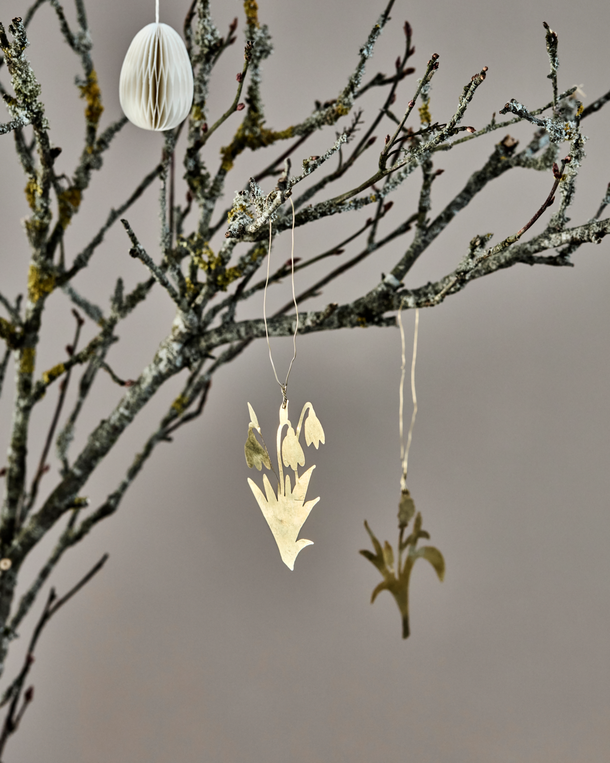 A bare branch displays House Doctor's Easter ornaments—Set of 3 Lilly Flowers in Brass—elegant, handcrafted metal decorations against a neutral background.