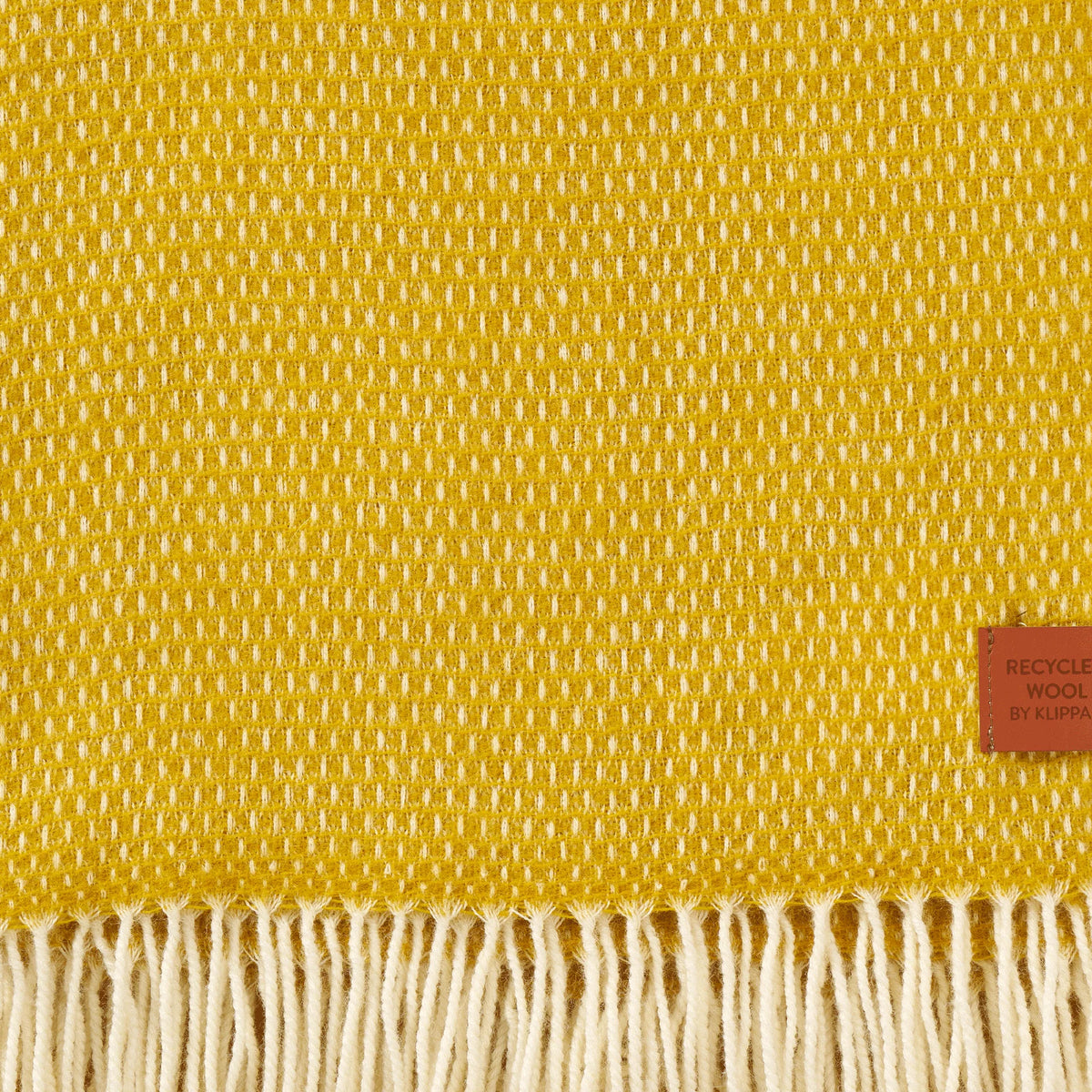 Woven in a saffron yellow and white grid pattern and finished with cream-colored fringed tassels, the Hugo Recycled Merino & New Merino Brushed Throw by Klippan Yllefabrik combines sustainability with luxurious softness. Expertly crafted from a blend of recycled and new merino wool, this elegant throw features a small brown label on the lower right corner that reads “RECYCLED WOOL BY KLIPPAN,” making it an exquisite accent for your home décor.