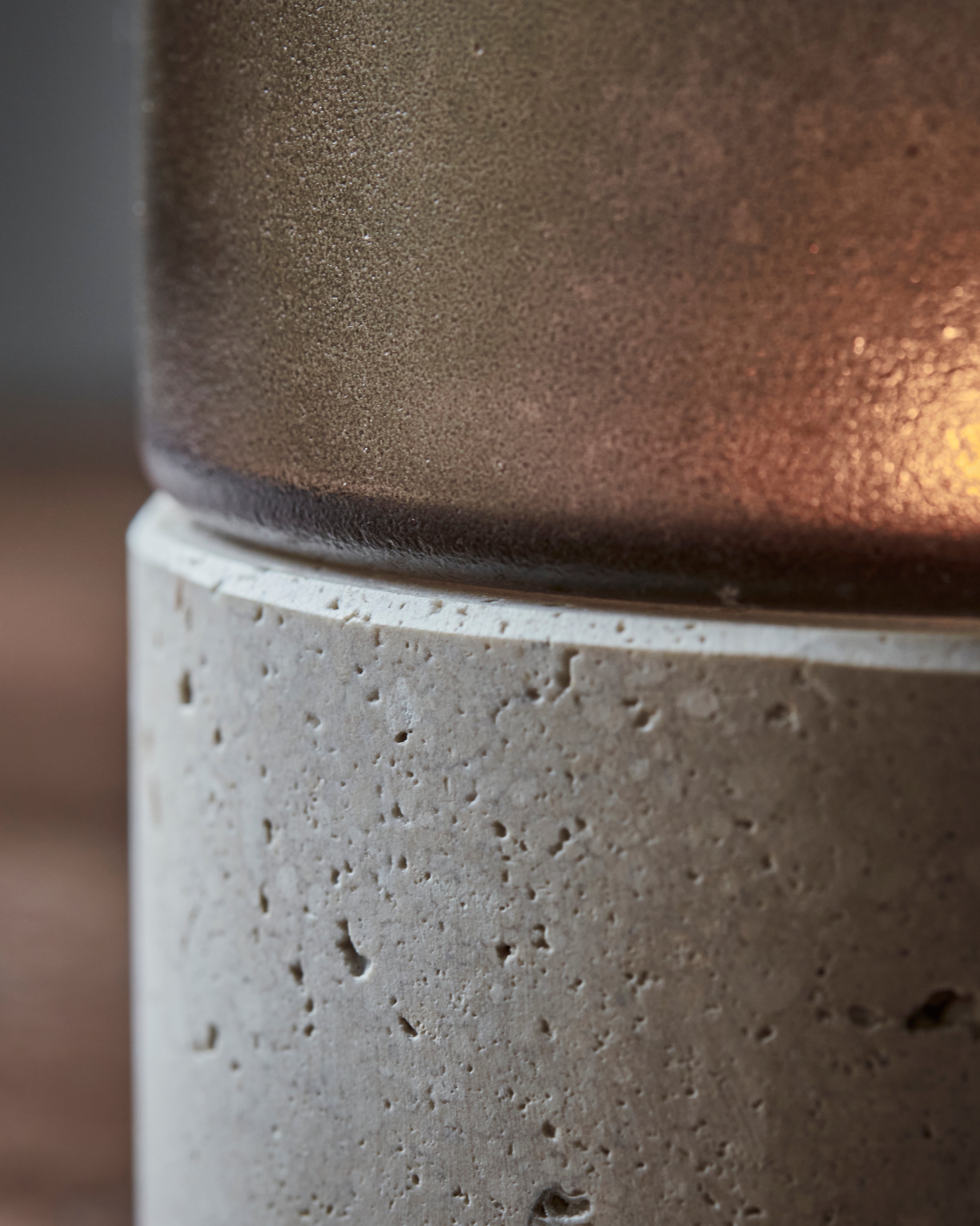 Close-up of the House Doctor Candle Holder Rivo w. Brown Glass, Handmade, showcasing its cylindrical form with a textured travertine stone base and a frosted, translucent brown mouthblown glass upper section, highlighting surface details and subtle lighting.