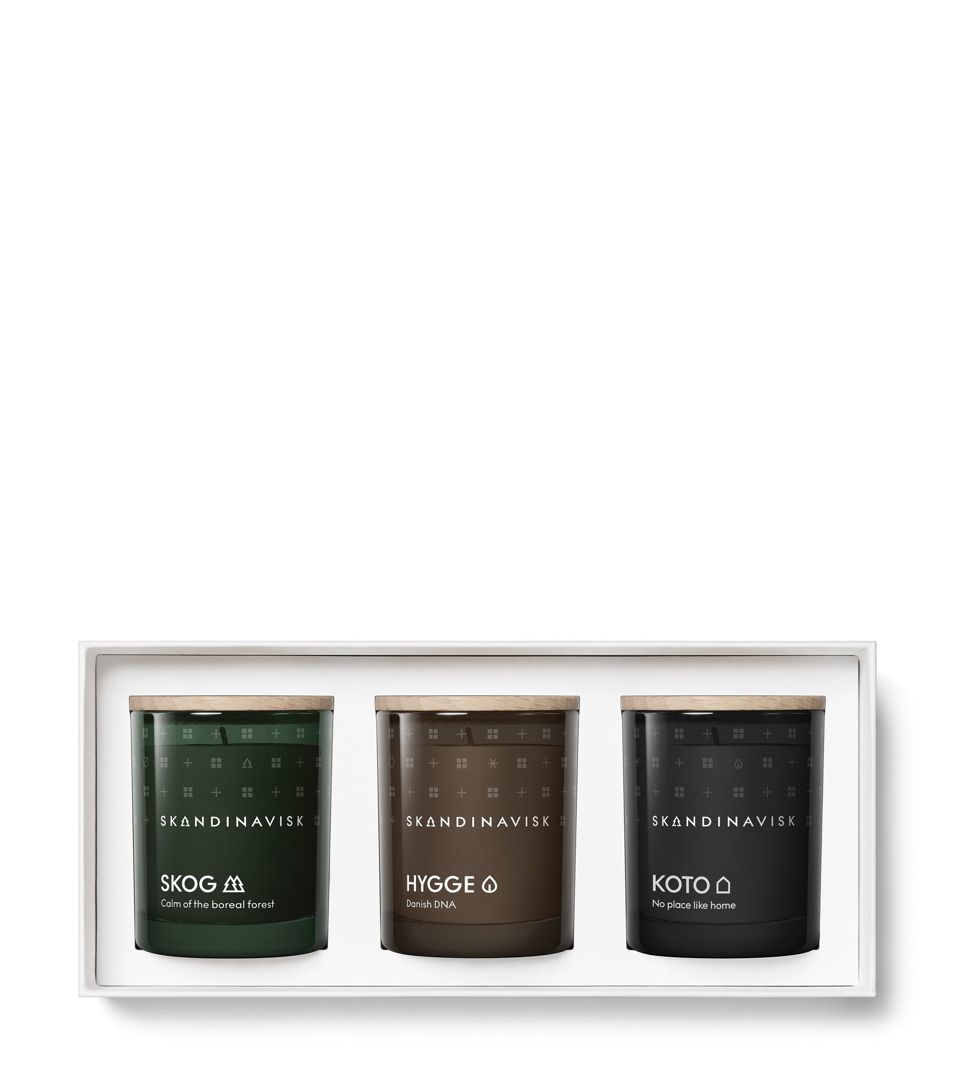 The Skandinavisk Giftset Scented Candles Hibernate features three mini candles—Skog (green), Hygge (brown), and Koto (black)—each crafted from Swedish rapeseed wax and presented side by side in a sleek white box with wooden lids.