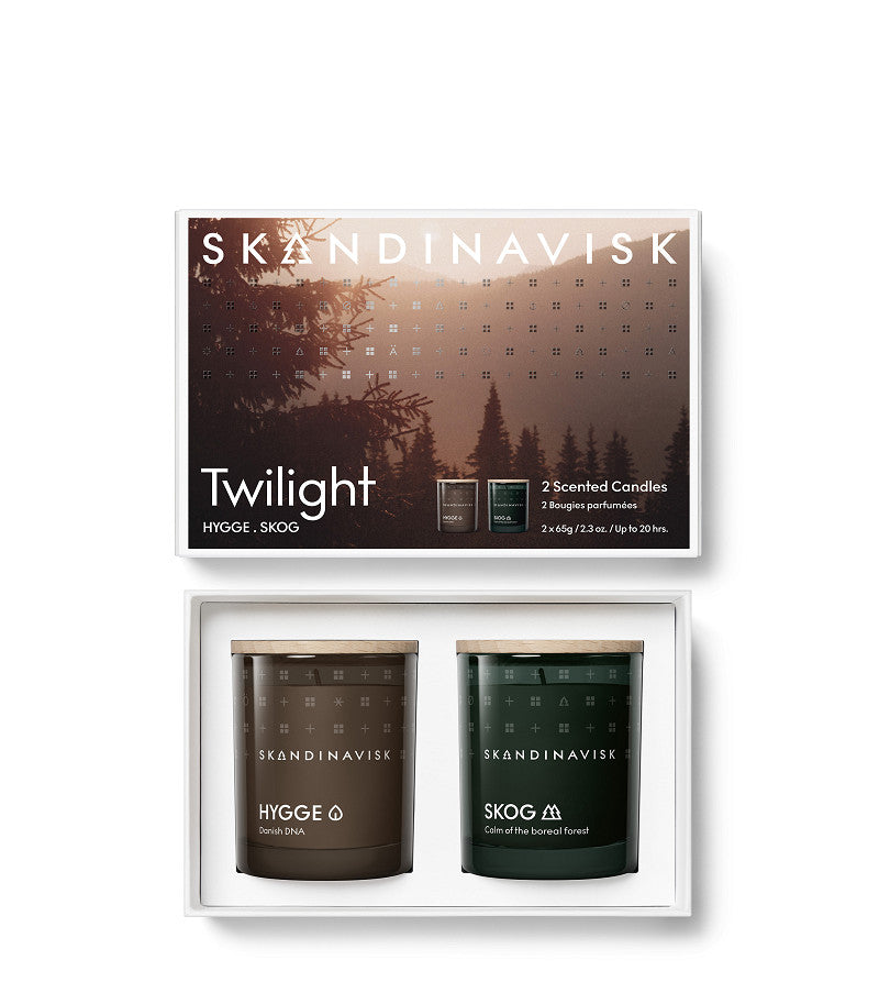 A boxed set titled Giftset Scented Candle Twilight w. 2 Mini Candles Skog & Hygge by Skandinavisk features two mini scented candles—SKOG (green) and HYGGE (brown)—housed in elegant glass jars. Presented against a backdrop of pine trees and a dusky sky, this beautiful set encapsulates the comforting ambiance of Scandinavian forests, making it perfect for infusing any space with the tranquility of nature.