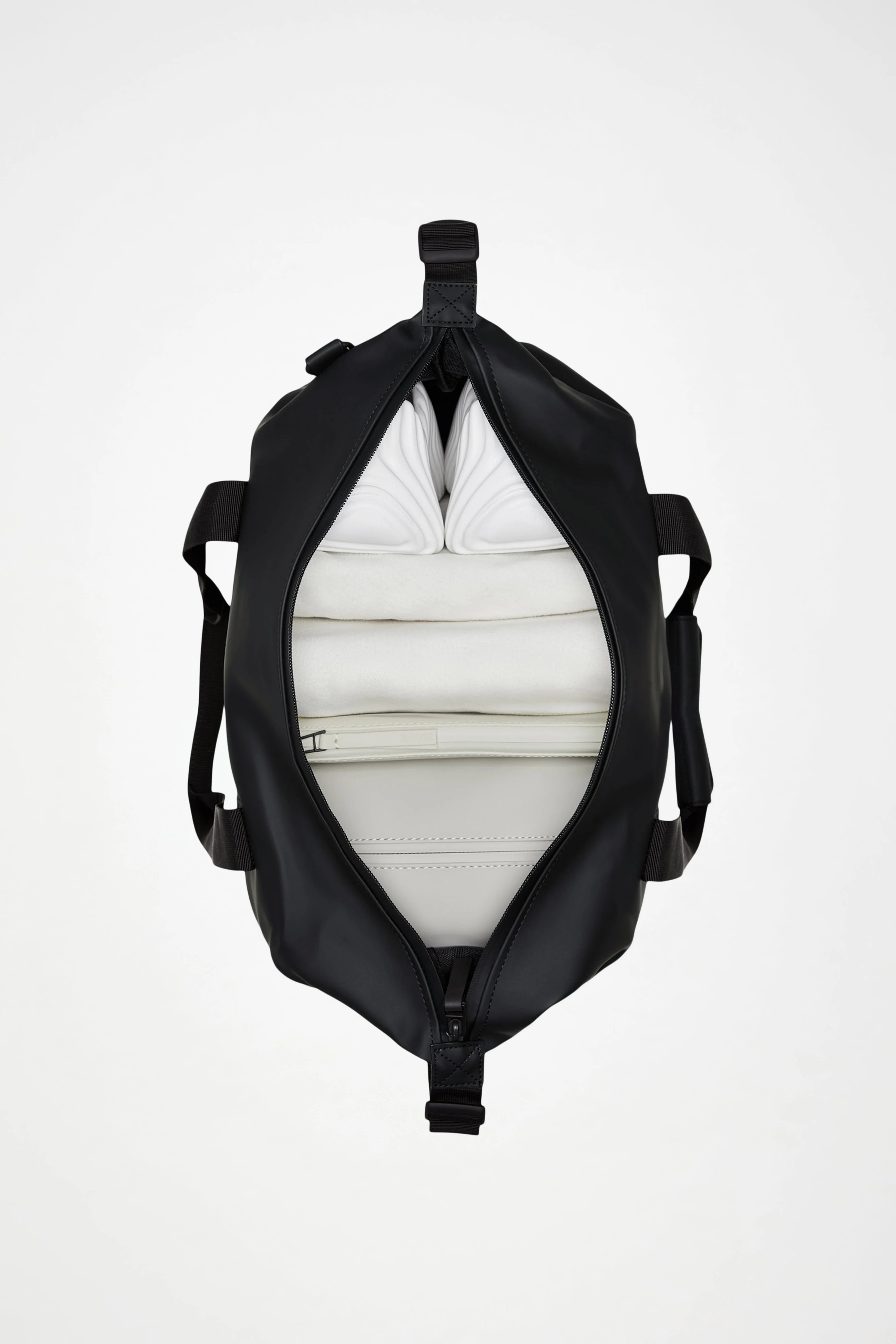Top view of an open Rains Hilo Weekend Bag Small in Navy, featuring a white interior with neatly packed white folded clothes and a zippered pocket inside, set against a plain white background—perfect as a compact travel bag or waterproof overnight bag from Rains for short getaways.