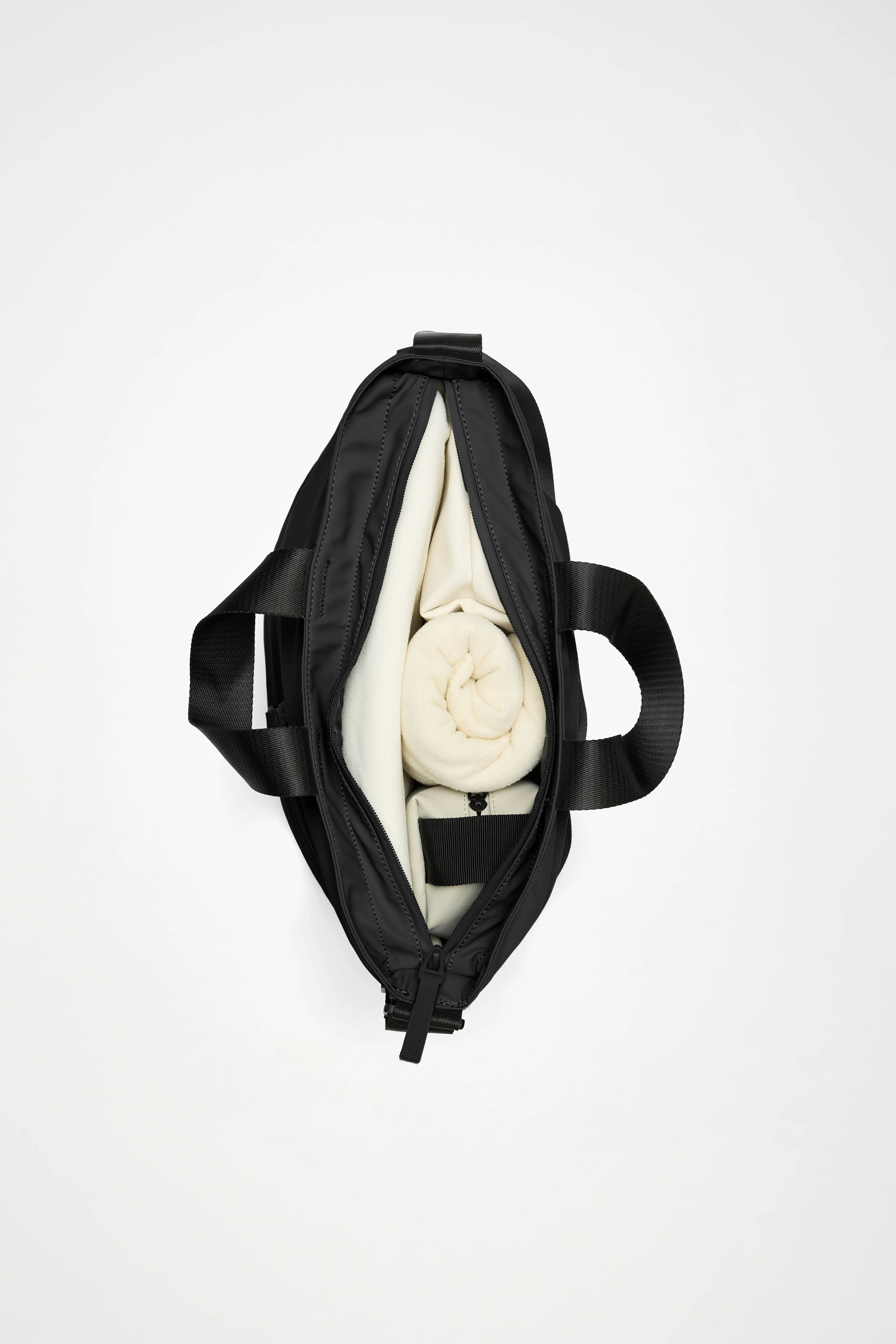 The Rains Dash Tote Bag in Black by Rains is shown from above, partially unzipped to display a rolled cream-colored towel and a folded cream item inside. It features an adjustable shoulder strap for comfortable carrying—making it the perfect everyday carryall, set against a white background.