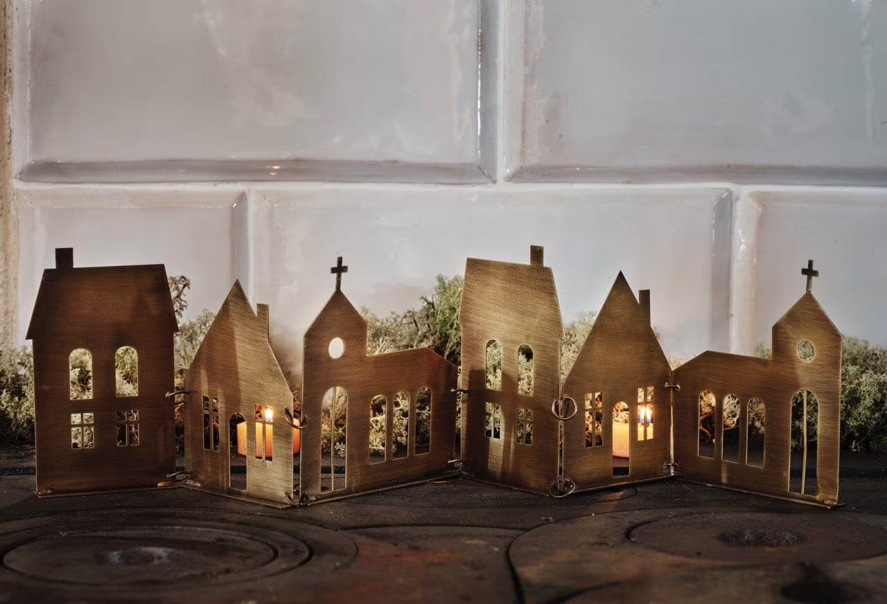 The Strömshaga Decorative Row City in Antique Brass features miniature houses and churches as a tealight holder, casting a charming city skyline silhouette and adding a cozy touch of decor to your space.