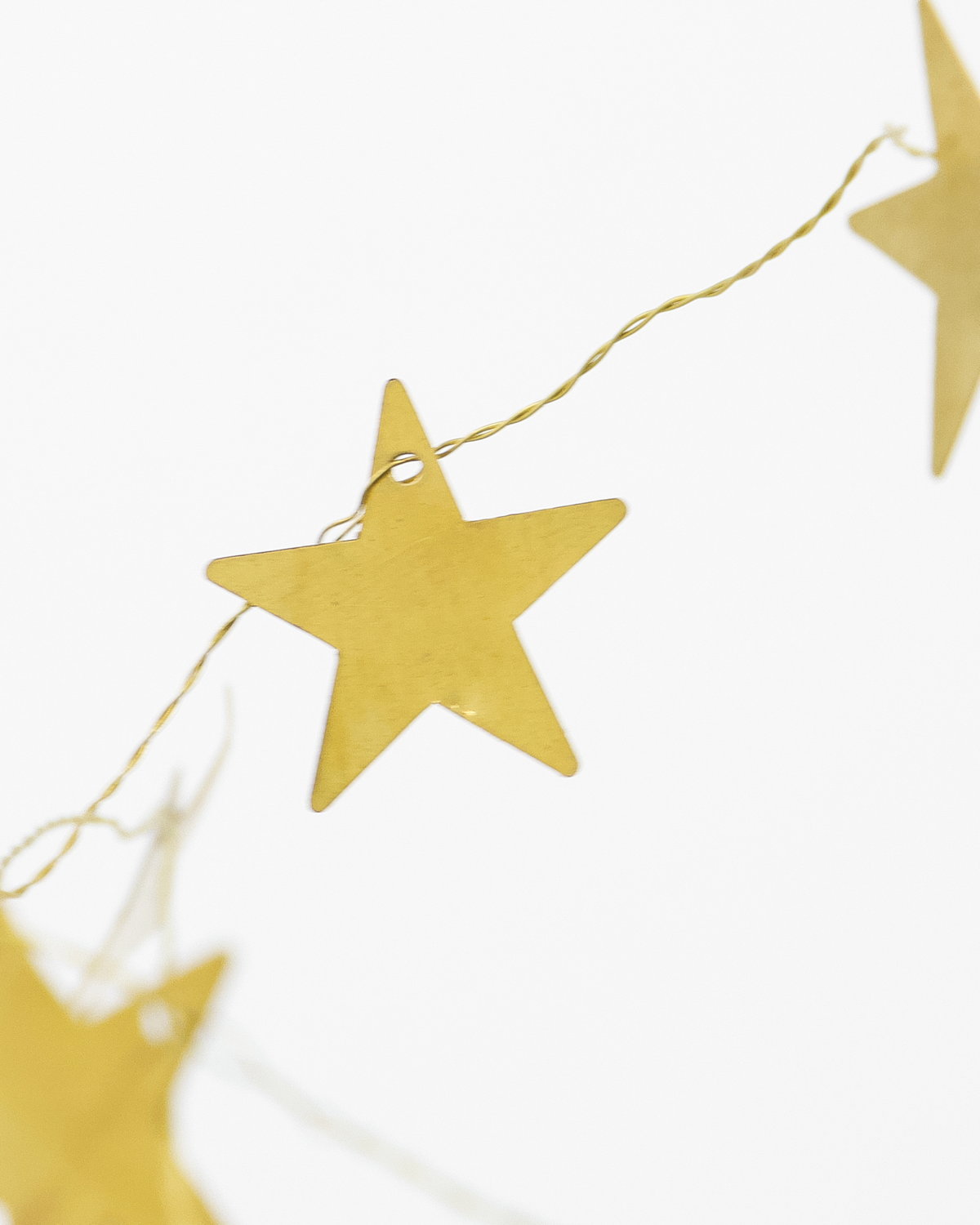A close-up of the House Doctor Garland Stars in Brass, 2.5 m, featuring brass star-shaped decorations on a string against a white background.