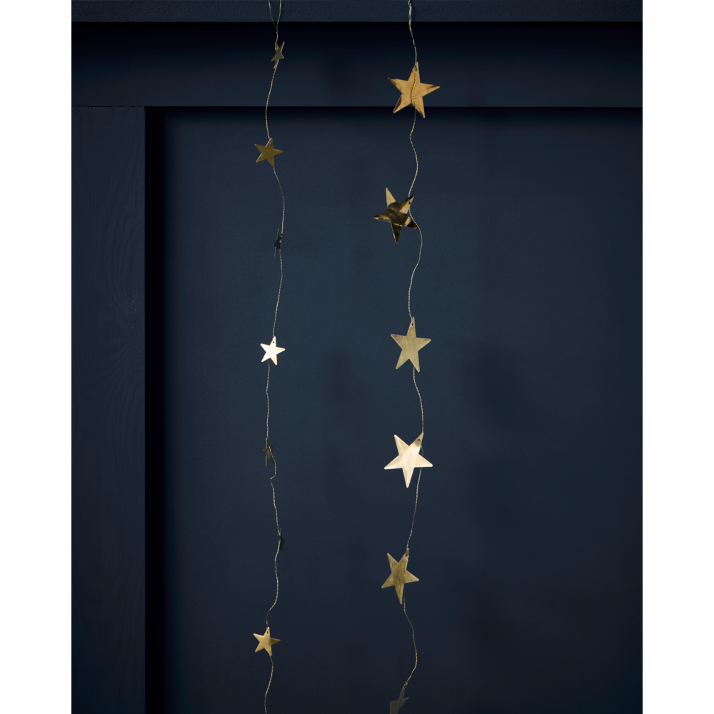 Two vertical Garland Stars in Antique Brass, 1.5 m, hang as handcrafted antique brass stars against a dark blue paneled wall.