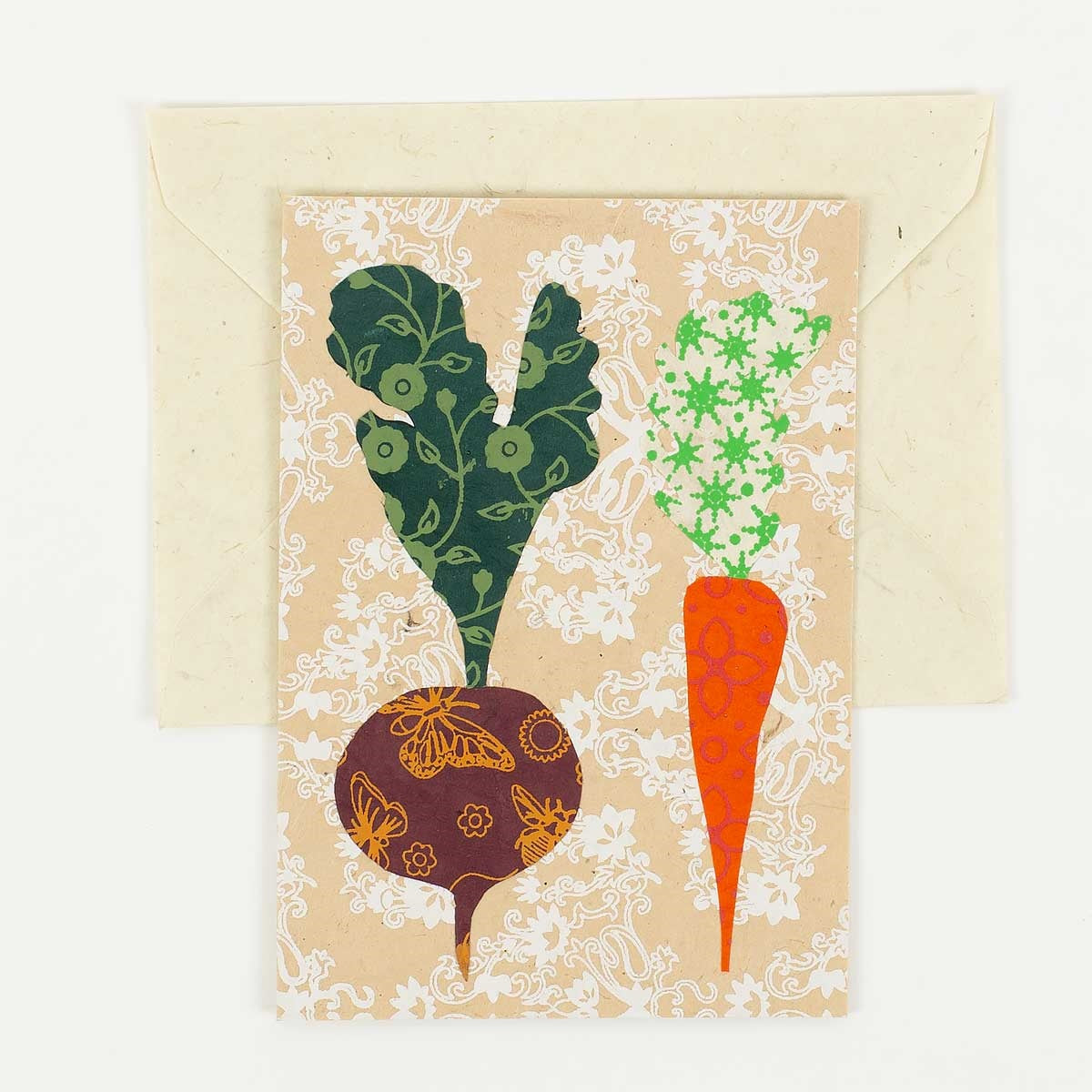 The Carrot & Beetroot Handmade Greeting Card by A World of Craft, featuring bold beet and carrot illustrations on a double-folded card, is displayed atop a cream-colored envelope against a plain white background.