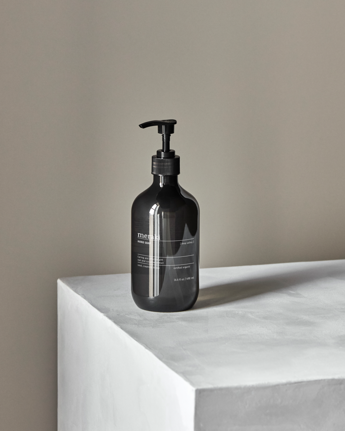 A black pump bottle of Meraki Hand Soap, Deep Valley, 490 ml sits on a minimalist white surface against a light gray background. Soft natural light highlights its refreshing fragrance, creating an elegant and modern scene with no other objects present.