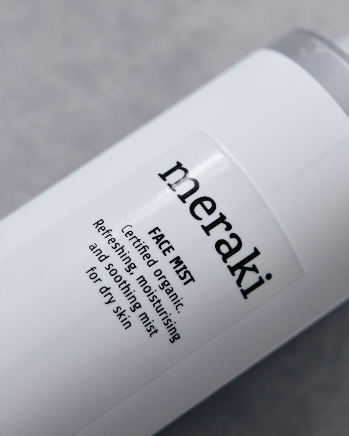Close-up of a white bottle labeled “Meraki Face Mist, Organic with Earth Marine Water.” This certified organic face mist is formulated to moisturize and soothe dry skin, helping you achieve a radiant complexion. The background appears softly blurred.