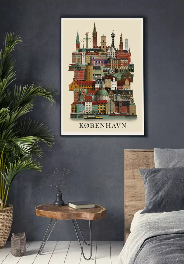 The Martin Schwartz Poster Copenhagen City A3, showing a colorful city skyline, is framed and hangs above a wooden side table with a vase and book, next to a green plant and gray bed against a dark gray wall.