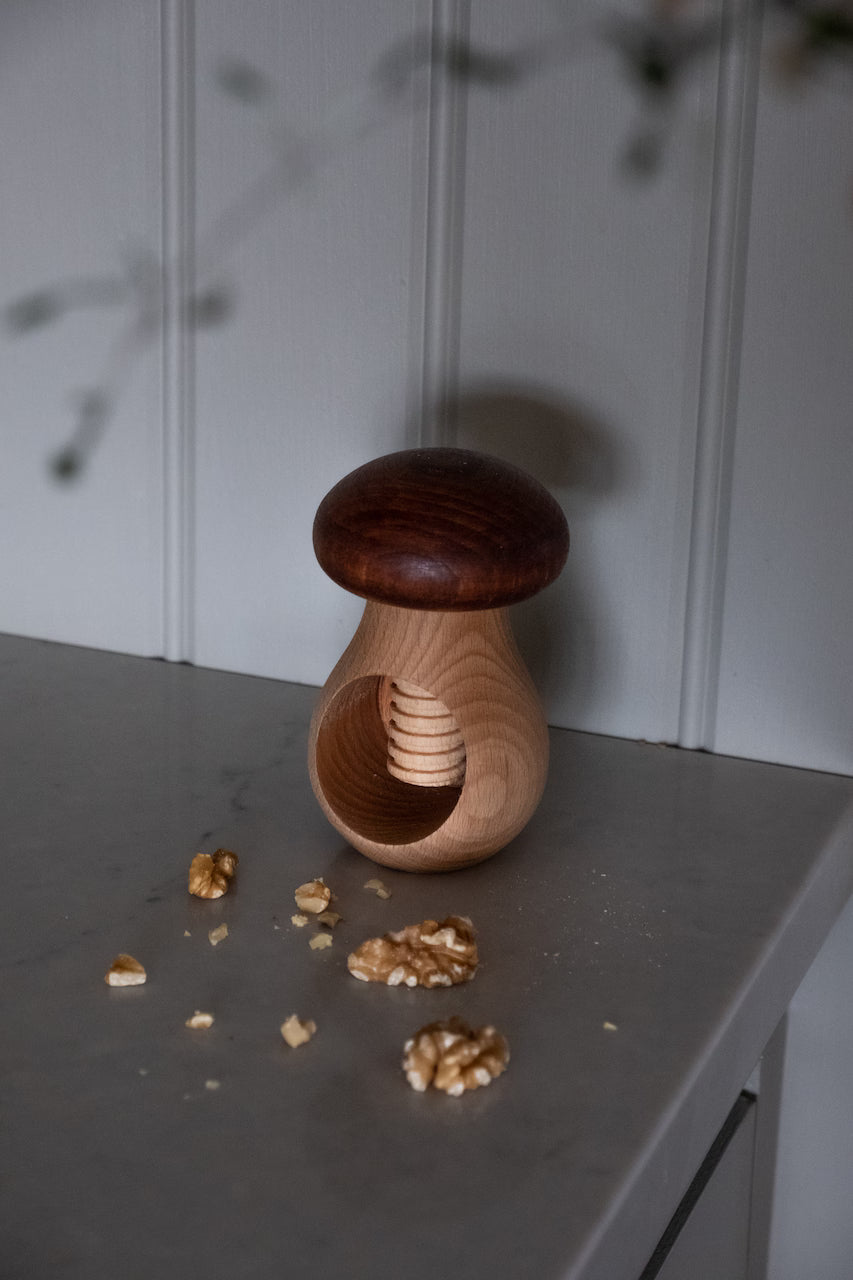 A Strömshaga Nutcracker Mushroom, Brown in Beech Wood, sits on a gray countertop surrounded by cracked walnut pieces.