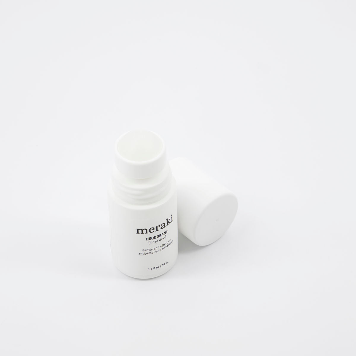 A white roll-on bottle of Meraki Organic Deodorant, Linen Dew, stands upright with its cap beside it on a plain white background, emphasizing its refreshing formula made with organic extracts.