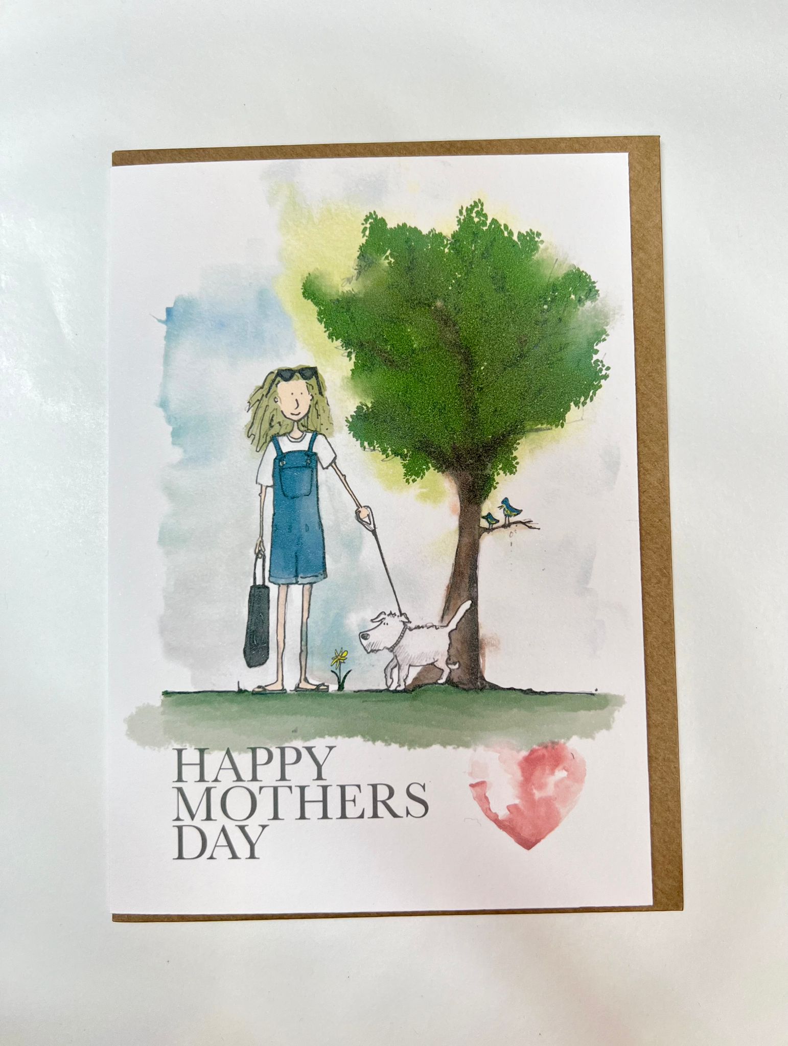 Blåbär Nordic Living’s Mothers Day Card - Dog Mum features a woman walking her white dog under a leafy tree with a bird, plus "Happy Mothers Day" and a pink heart—perfectly handcrafted for dog-loving mums.