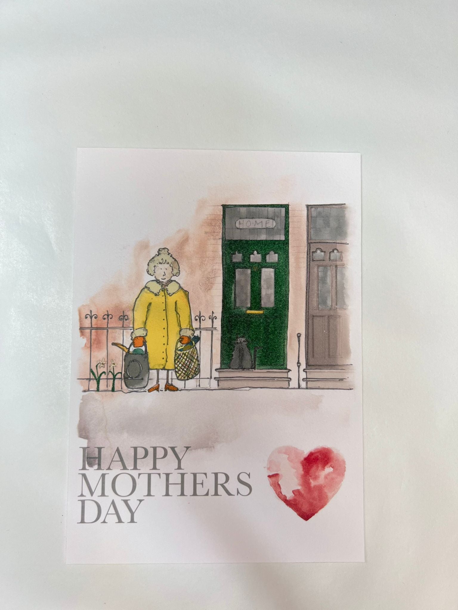 The Blåbär Nordic Living "Mothers Day Card - Shopping Mum" features a watercolor of an elderly woman in a yellow coat with shopping bags by a green door, plus "Happy Mothers Day" with a red heart—Nordic-inspired and perfect for Mother's Day.