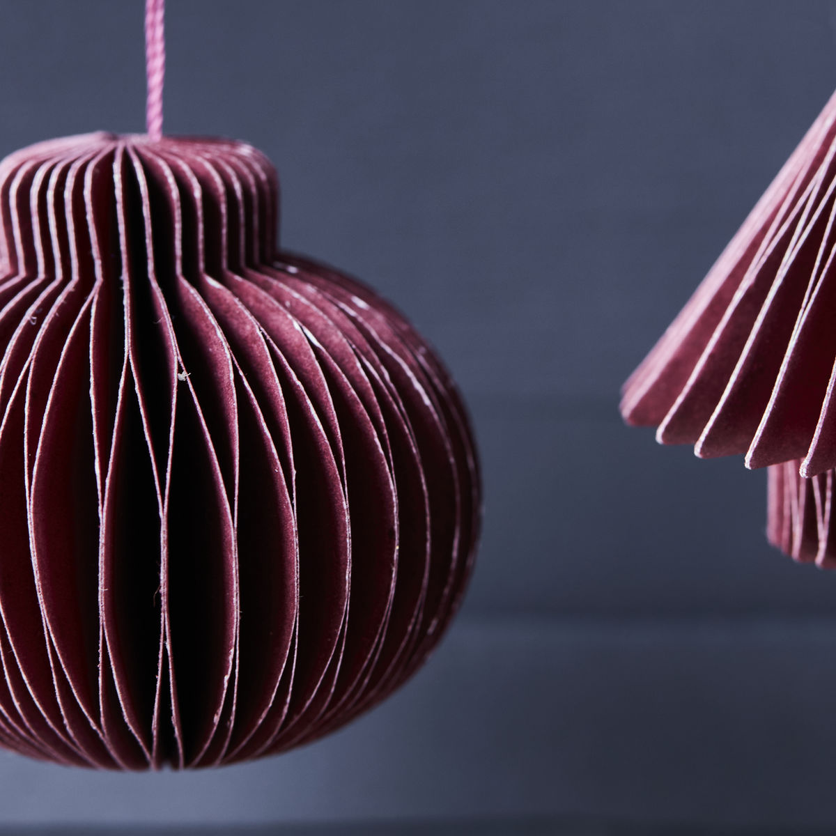 A close-up of two burgundy Ornament Comb paper ornaments from House Doctor (set of 6) hanging against a dark blue background, bringing a vintage-inspired accent to your Christmas décor.