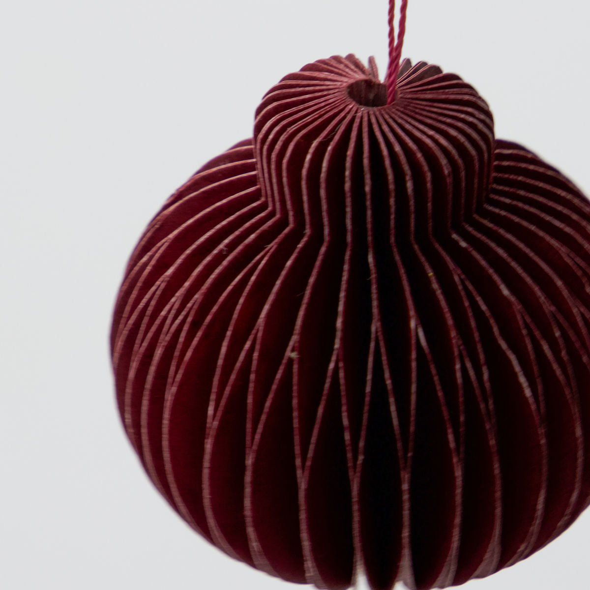 A close-up of House Doctor’s Ornament Comb in Paper, Burgundy (Set of 6), a vintage-inspired Christmas ornament hanging by a string against a white background—ideal for adding timeless charm to your décor.