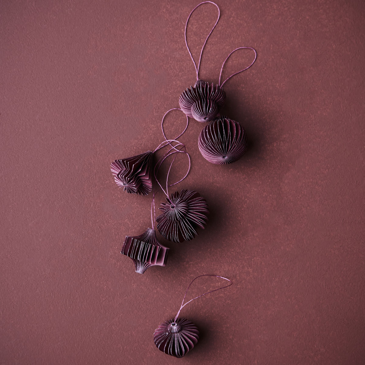 The House Doctor Ornament Comb in Paper, Burgundy, Set of 6 features vintage-inspired ornaments with string loops on a textured burgundy background—perfect for adding festive flair to your Christmas décor.