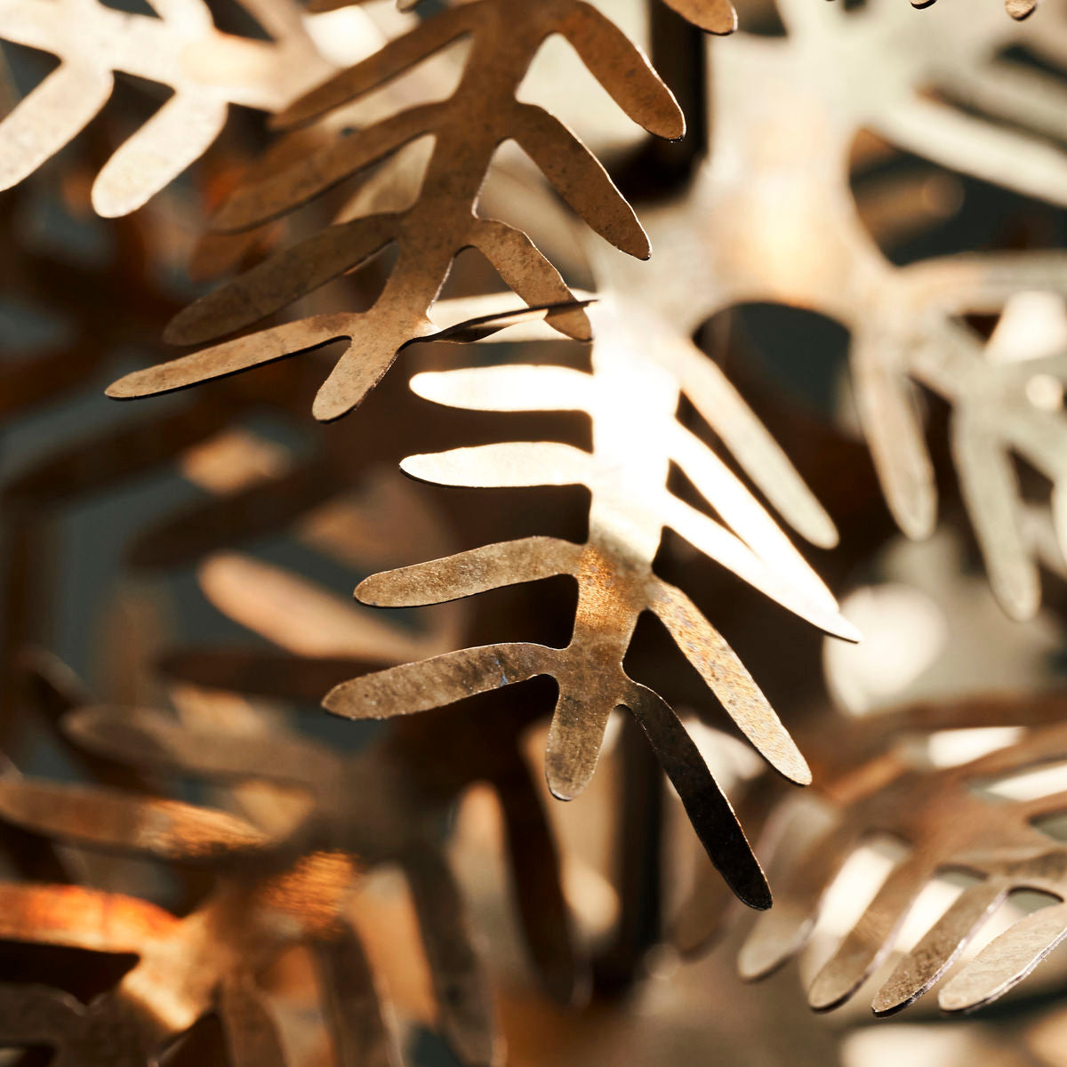 Close-up of Lamet Christmas Tree Ornaments by House Doctor—a set of 3 antique brass leaves with delicate cut-out shapes—illuminated by warm light, creating a festive interplay of highlights and shadows.