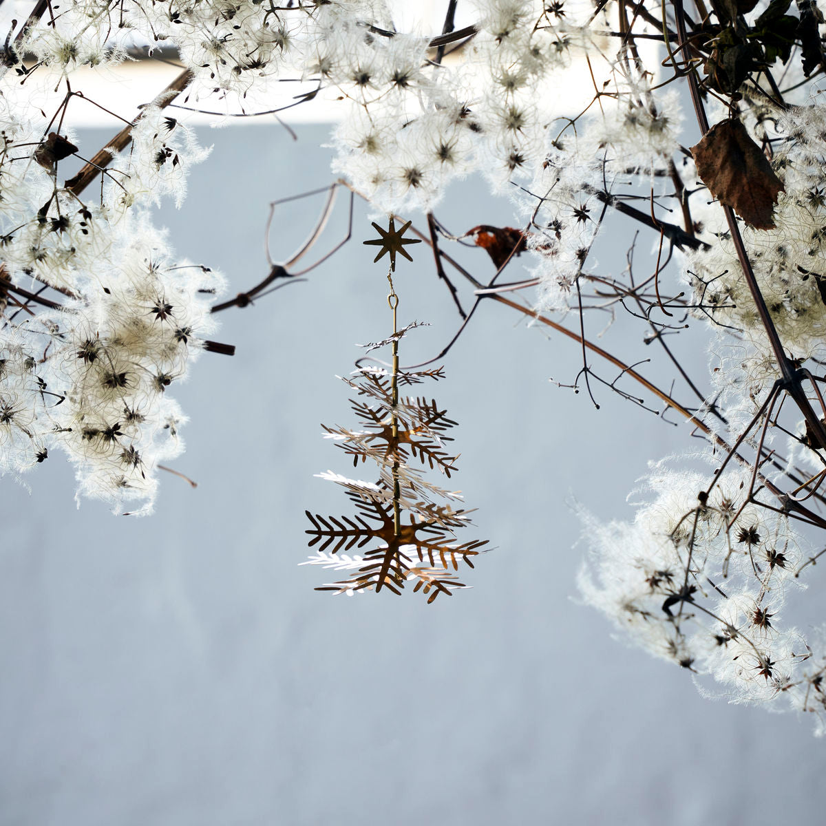 The Lamet Christmas Tree Ornaments by House Doctor, in antique brass and snowflake-shaped, add an elegant golden touch to your décor. Set of 3 displayed among white seed pods and leaves against a soft blue background.