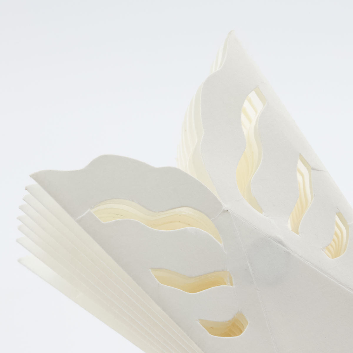 Close-up of an open book with thick, white pages featuring decorative wavy cut-outs—a festive touch inspired by House Doctor’s Paper Snowflake Ornaments, Set of 4, perfect for unique Christmas décor.