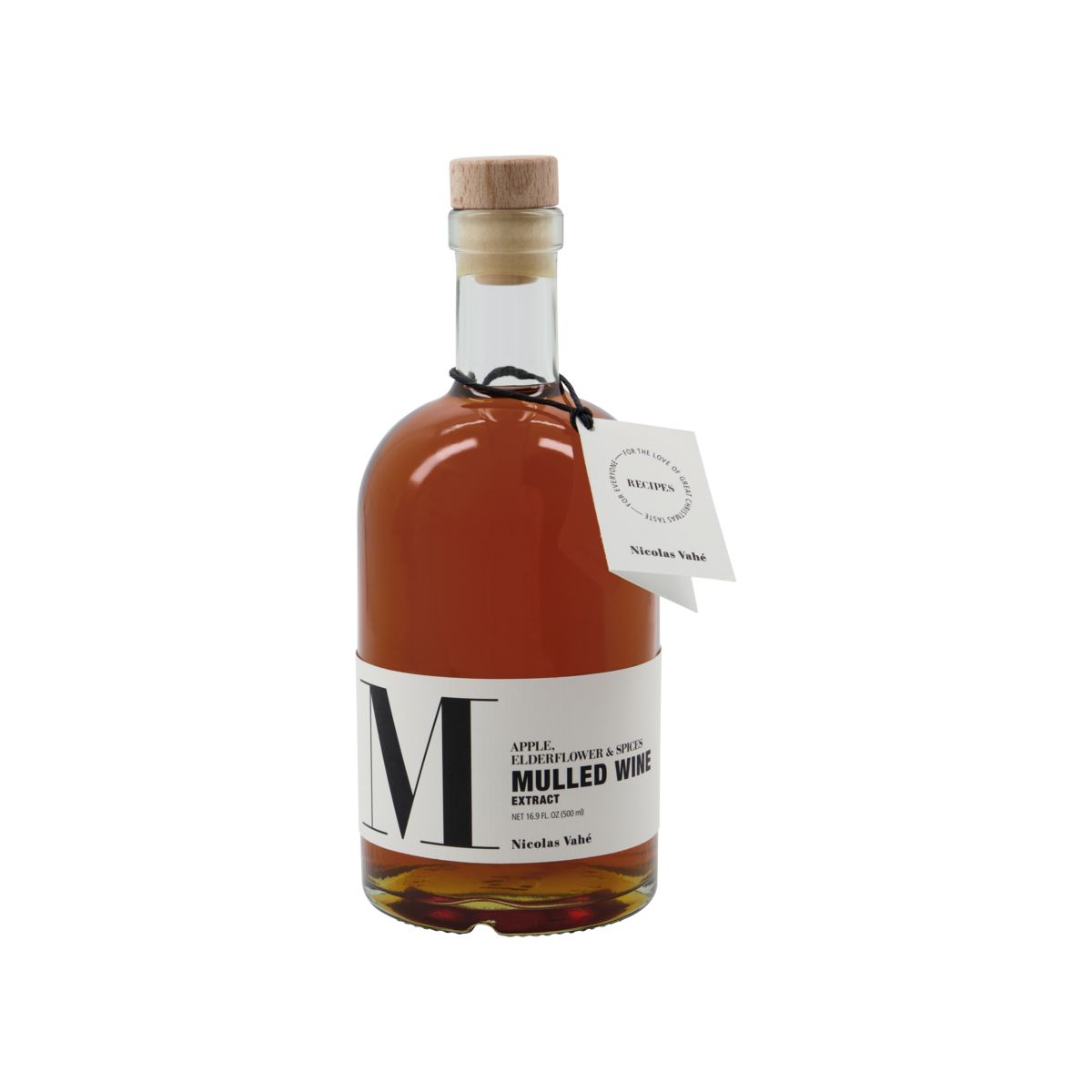 A clear glass bottle from Nicolas Vahé, topped with a wooden cork, holds amber Mulled Wine Extract – Apple, Elderflower & Spices – featuring a large “M,” a hanging tag, and festive hints of elderflower.