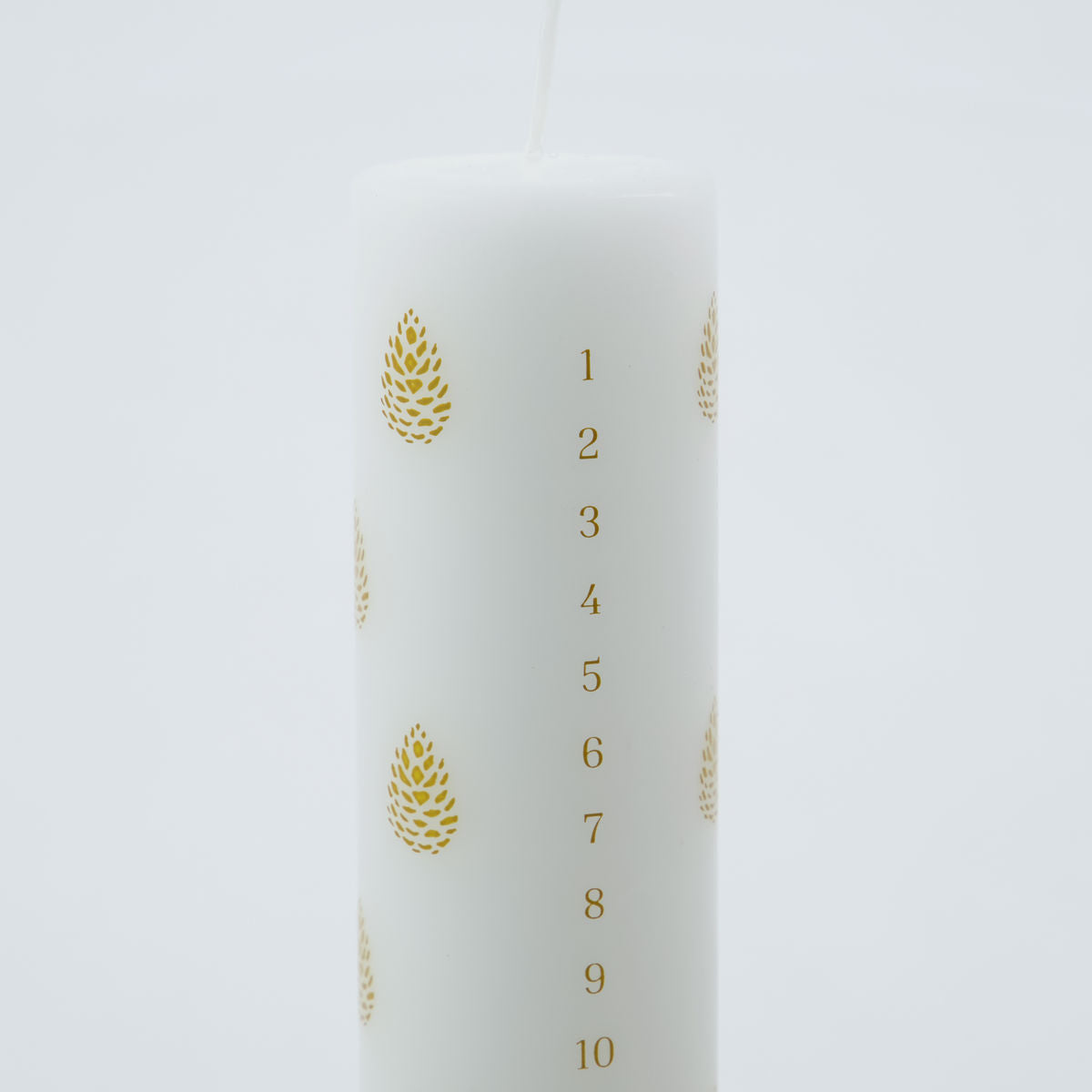 The House Doctor Calendar Candle 24 days of Christmas features a white pillar design with gold pinecones and numbers 1 to 24 printed vertically, perfect for a festive countdown.