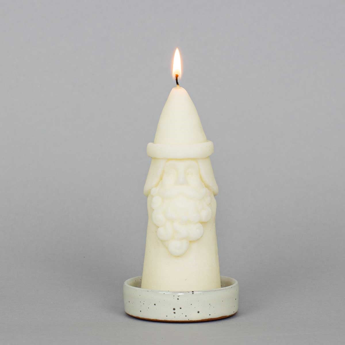 Lit cone-shaped handcrafted Santa Candle molded into the form of Santa Claus, sitting on a small speckled ceramic plate.