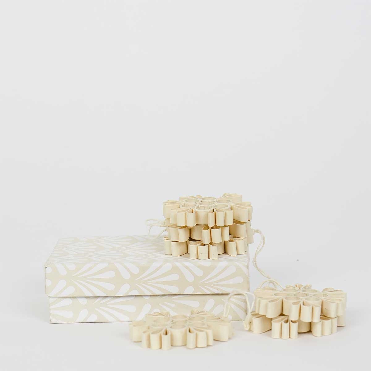 A World of Craft Quilled Snow Flake Christmas Ornaments, 6 Pack in Beige, displayed atop a decorative white leaf-patterned box, add handmade, eco-friendly charm to any setting.