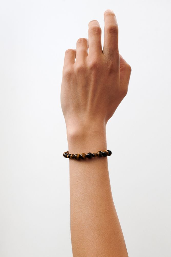 A hand with a raised wrist wears the Pernille Corydon Earth Bracelet w. Tiger Eye Stones, crafted from polished brown and black Tiger Eye, against a plain white background.