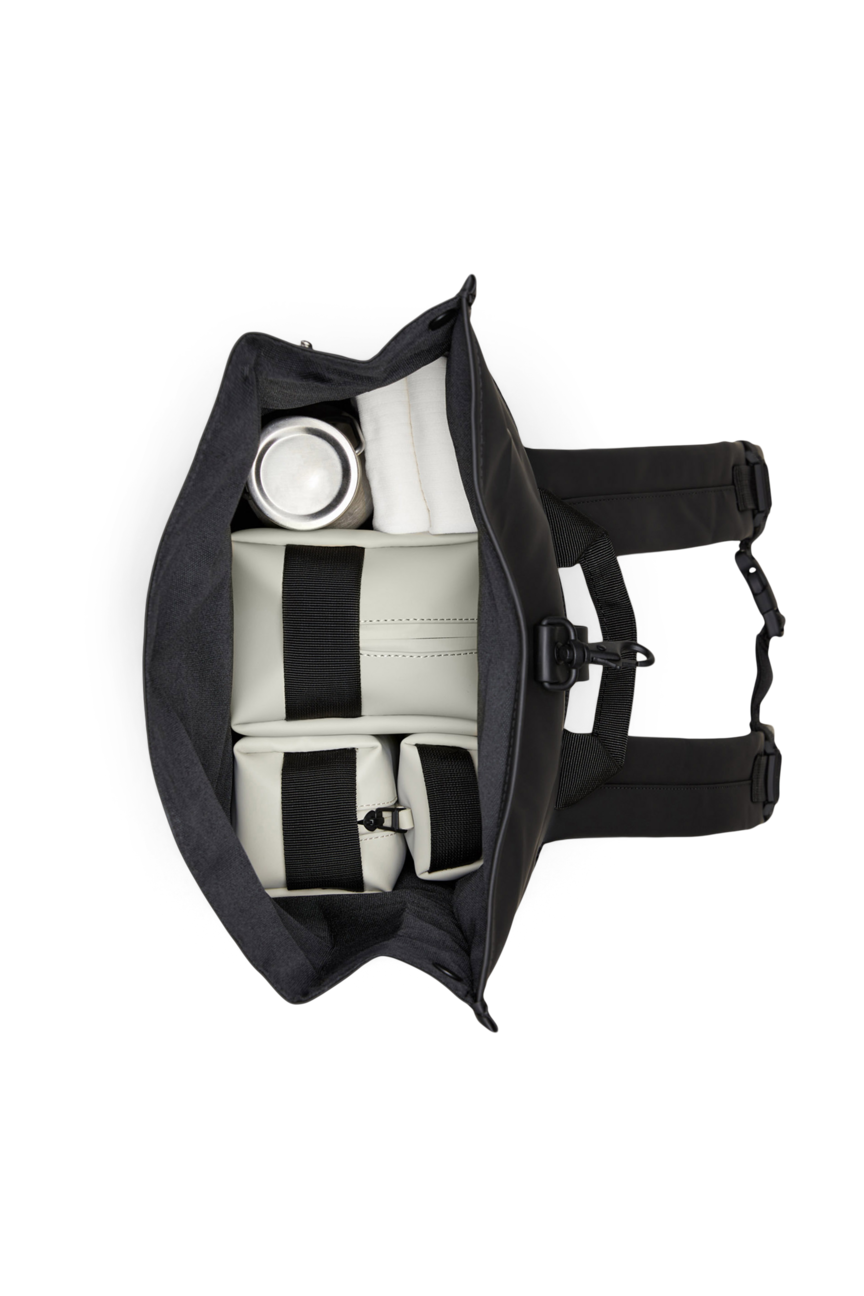 Top view of an open Rains Rolltop Rucksack Backpack in Black by Rains, displaying its organized waterproof interior with compartments neatly holding a water bottle, a rolled towel, and two rectangular pouches, all set against a white background.