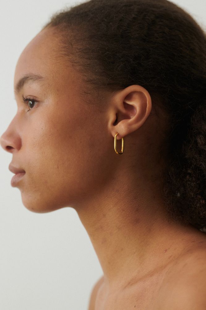 A close-up side profile of a woman with curly hair wearing Pernille Corydon's Soft Edge Huggies in Silver, set against a plain light background.
