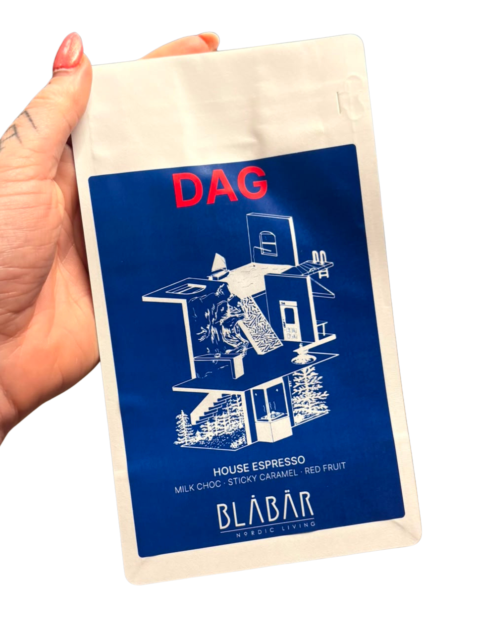 A hand holds a blue and white Dag House Coffee Beans Blåbär bag (Single Origin Colombia, 250g) by Blåbär Nordic Living, featuring a modern line drawing and flavor notes of milk chocolate, sticky caramel, and red fruit.