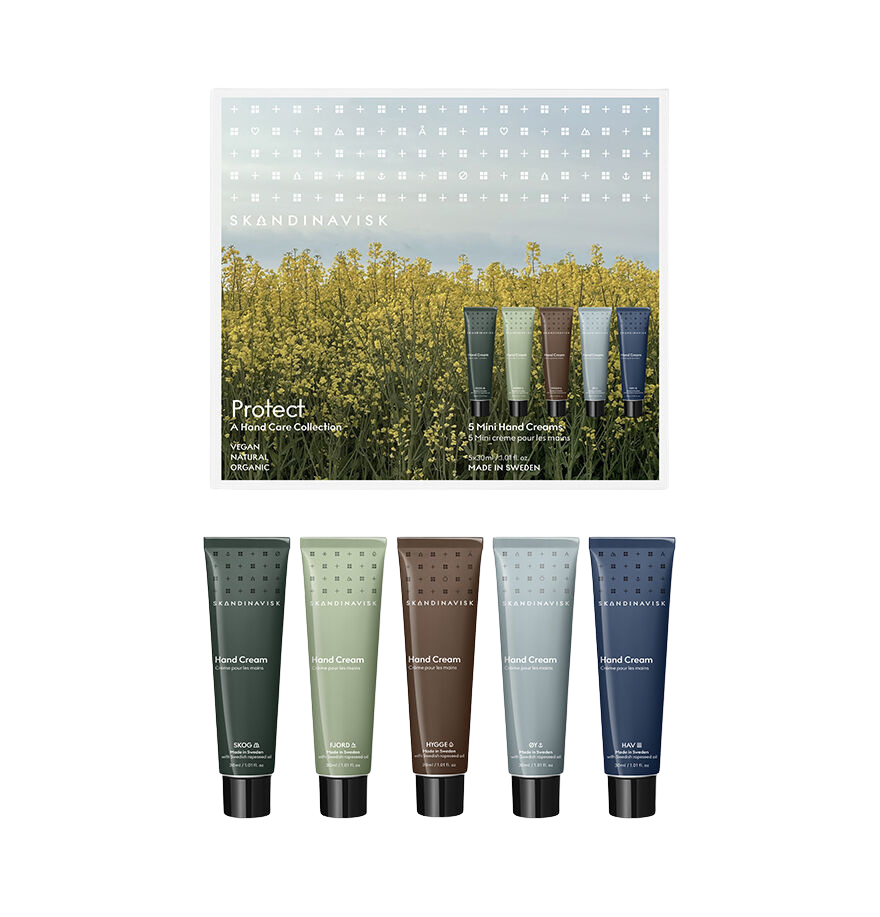 A set of five Skandinavisk Giftset Mini Hand Cream Protects—including Skog, Fjord, Oy, Hav, and Hygge—enriched with natural ingredients like organic aloe vera, in green, brown, gray, and blue tubes. They are displayed in front of a box featuring a yellow flower field and the product name "Protect.