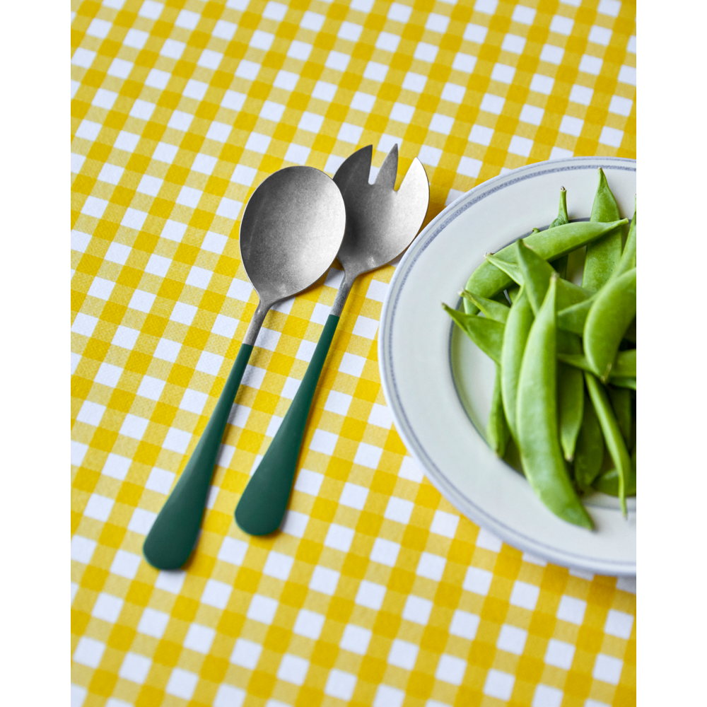 A plate of fresh snap peas sits next to the Nicolas Vahé Salad Set in Stainless Steel, Green, on a yellow and white checkered tablecloth.