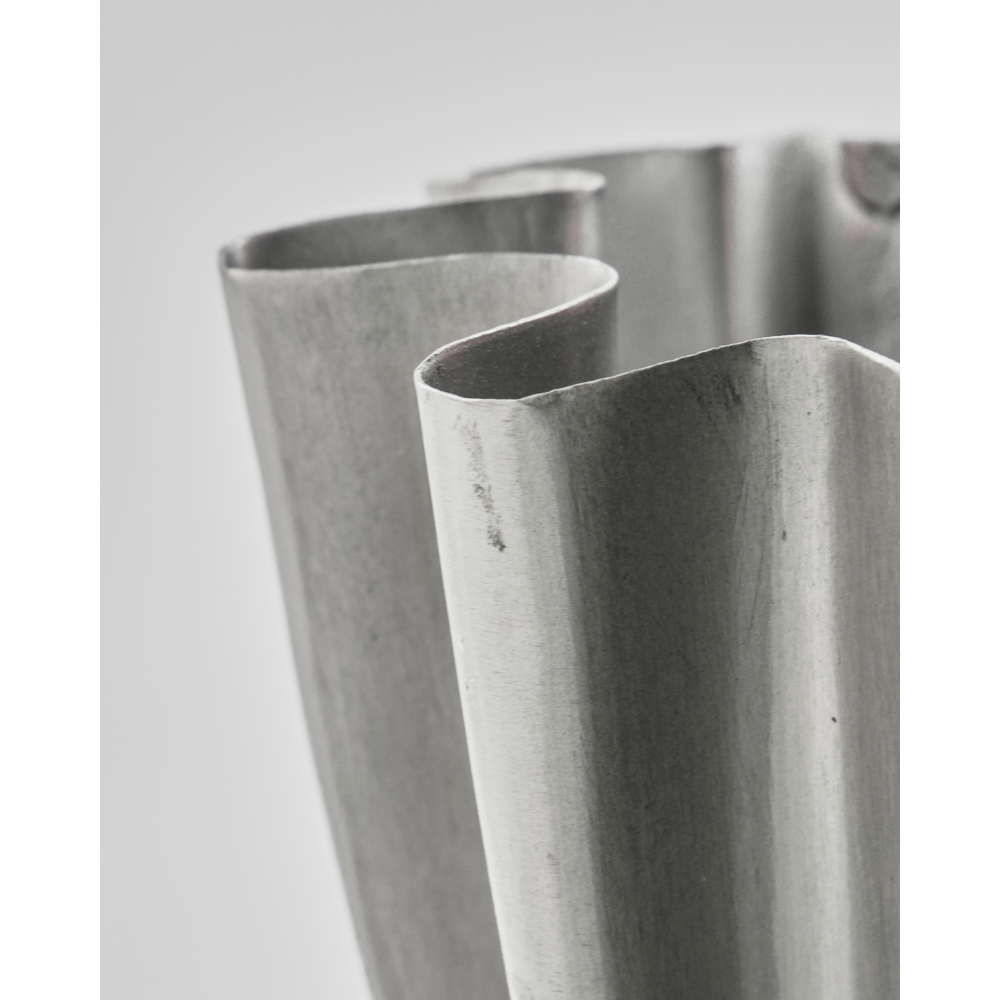 A close-up of the wavy, scalloped edge on the small Flood vase by House Doctor, featuring a brushed silver finish, brings modern flair to any room against a plain light gray backdrop.
