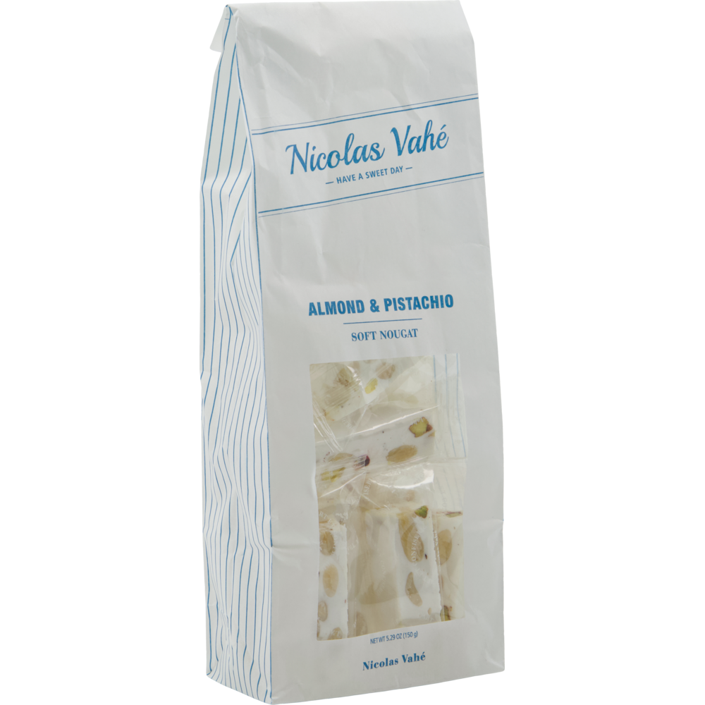 The Nicolas Vahé Soft Nougat, Almonds & Pistachios 150g comes in a white paper bag with a clear window showing nougat pieces filled with almonds and pistachios. Blue text and stripes give the packaging a charming look.