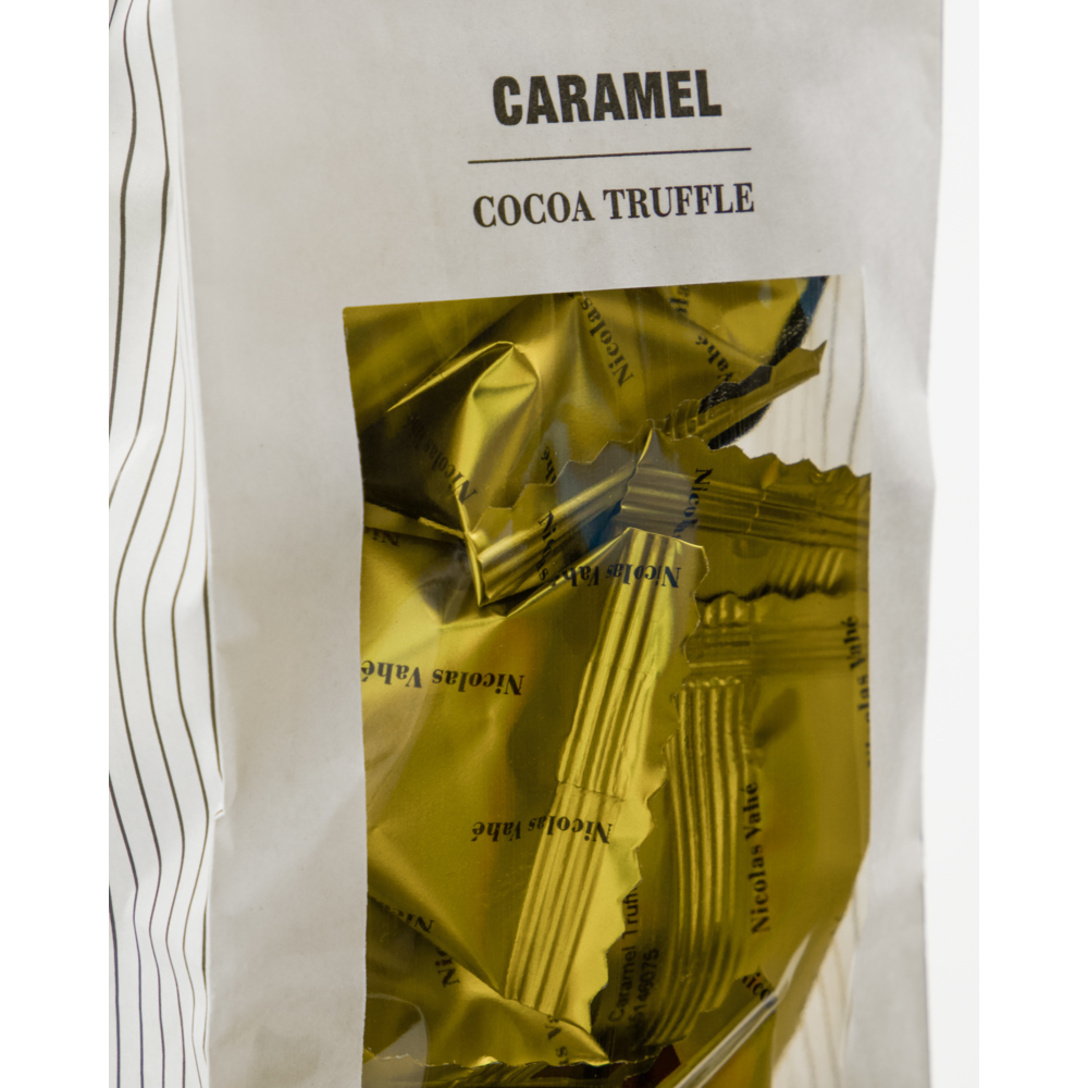 A close-up of a white Nicolas Vahé Cocoa Truffle, Caramel bag displays melt-in-your-mouth gold candies, individually wrapped and visible through a transparent window on the front of the packaging.