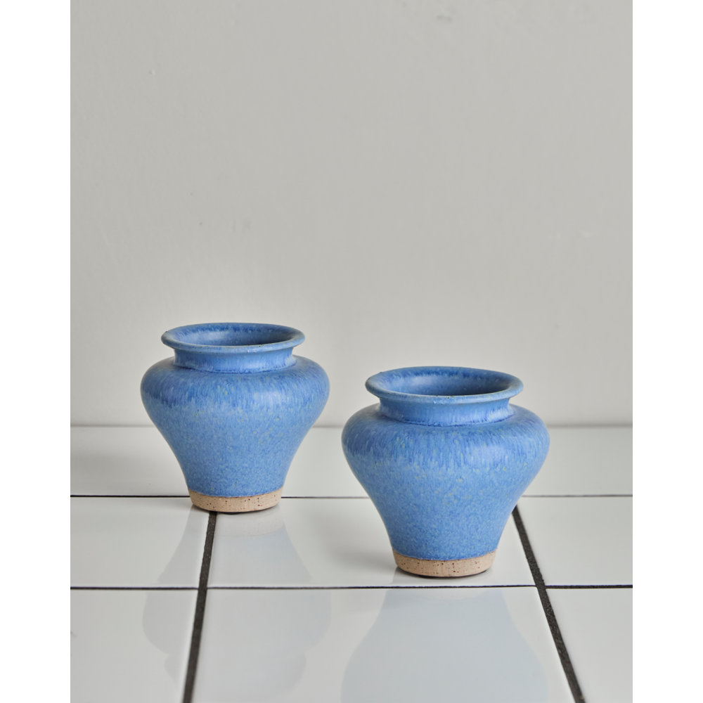 The House Doctor Vase Kolo Blue Set of 2 features small, round blue earthenware vases with wide openings and natural bases, displayed on glossy white tiles against a light gray backdrop.