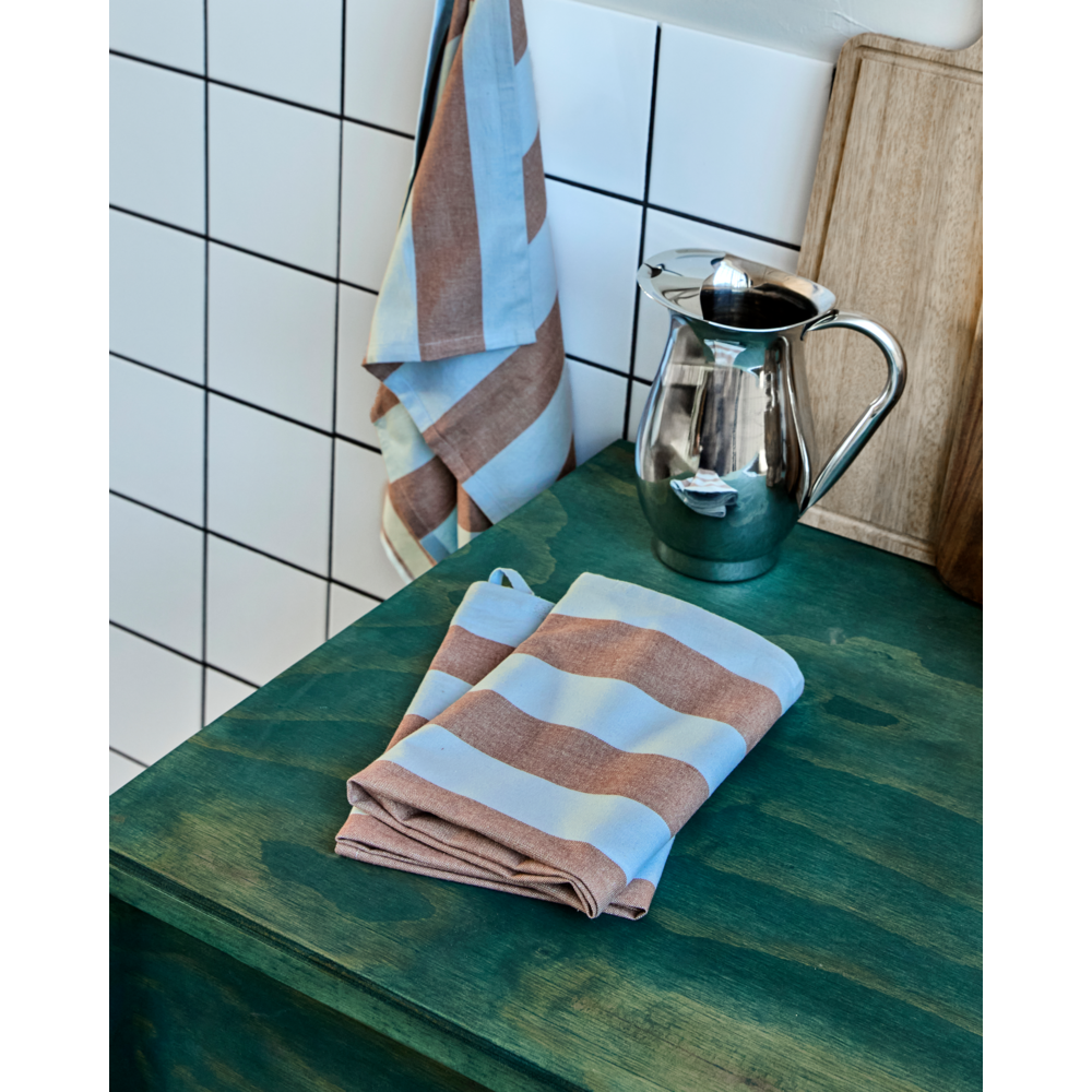 A folded and a hanging striped brown and light blue House Doctor Tea Towels Cook (Set of 3), plus a silver pitcher and wooden board on a dark green countertop with white tiled wall—perfect for showcasing these absorbent tea towels.