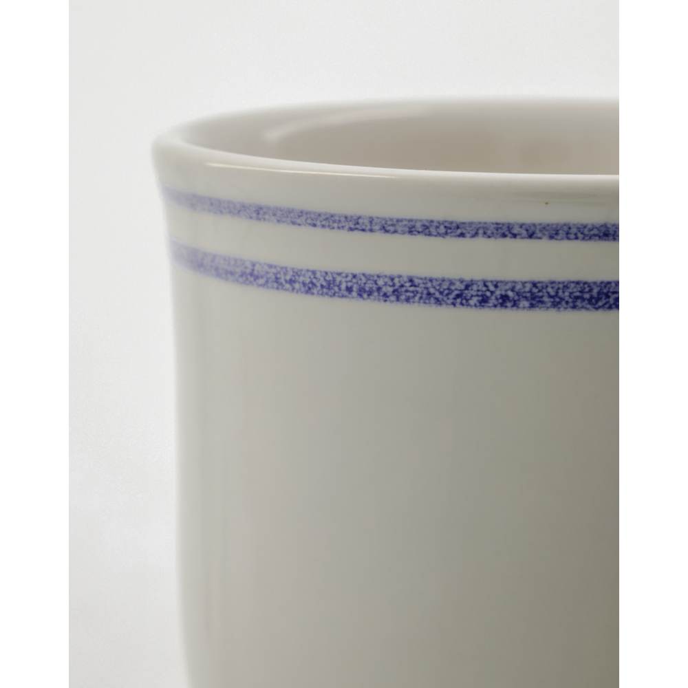 Close-up of the Nicolas Vahé Mug Bistro, Blue Line (Set of 2), a white ceramic mug with two blue speckled lines near the rim, set against a plain light background.