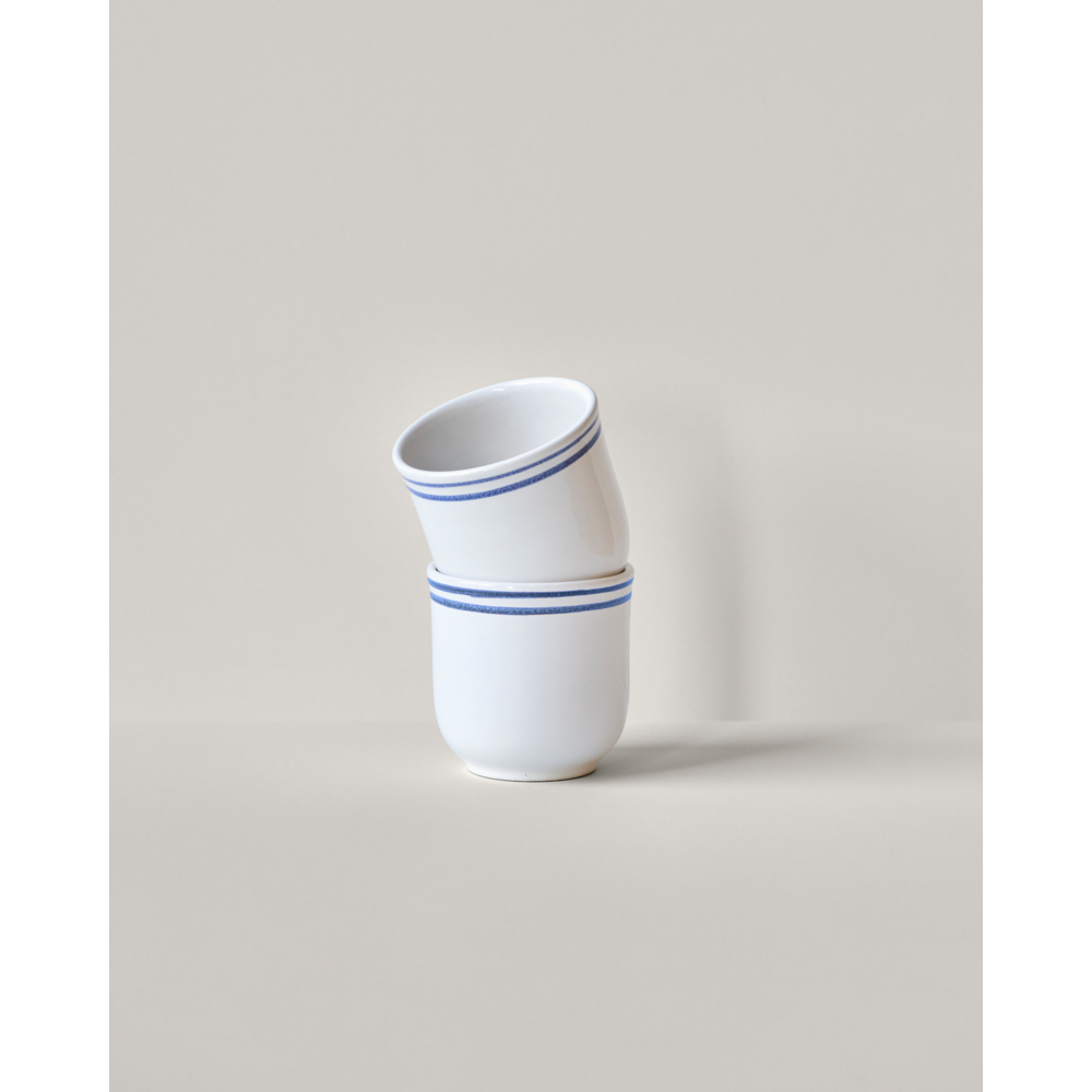 The Mug Bistro, Blue Line set of 2 by Nicolas Vahé features white stoneware mugs with blue rim stripes, shown stacked slightly askew against a plain light gray background.