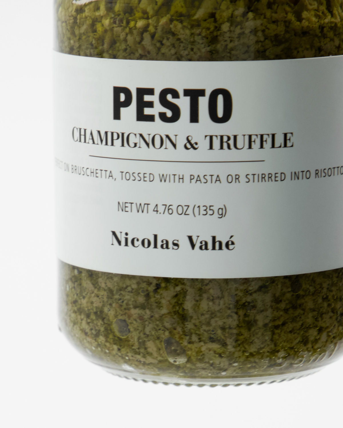 A close-up of a jar of Nicolas Vahé Pesto, Champignon & Truffle reveals green mushroom pesto inside. The label recommends enjoying this rich truffle pesto on bruschetta, pasta, or in risotto.