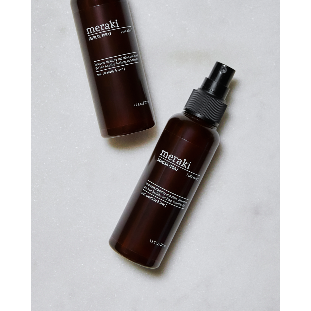 Two brown Meraki Refresh Spray Hair, Soft Allure bottles with black pumps are displayed on a white marble surface—one lying flat and the other positioned at an upright angle. These curl-friendly bottles feature minimalist white text and labels, ideal for anyone looking for a silicone-free hair refresher from Meraki.