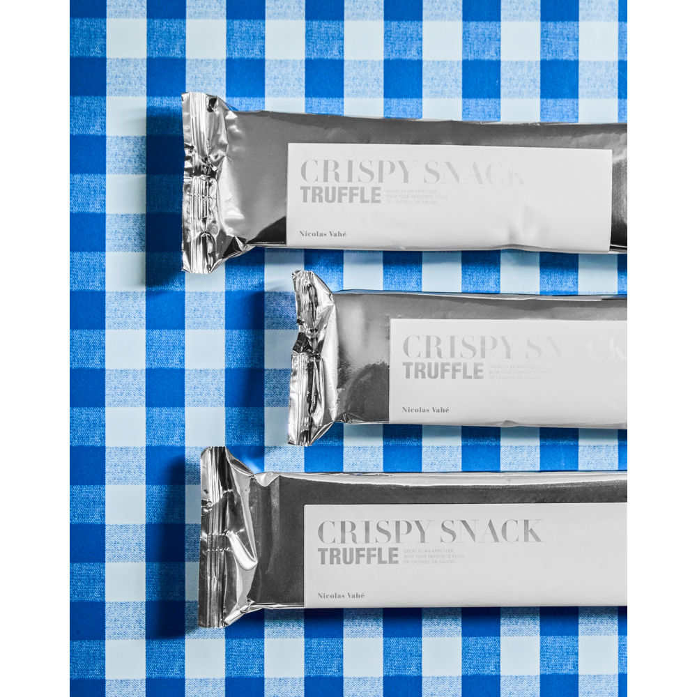 Three silver-wrapped Nicolas Vahé Crispy Snack bars, Truffle flavour, are arranged on a blue and white checkered surface. The minimalist packaging features simple text and a clean design that hints at the satisfying, crunchy texture inside.